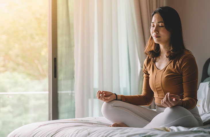 A woman sits on her bed and reaps the values of meditation.