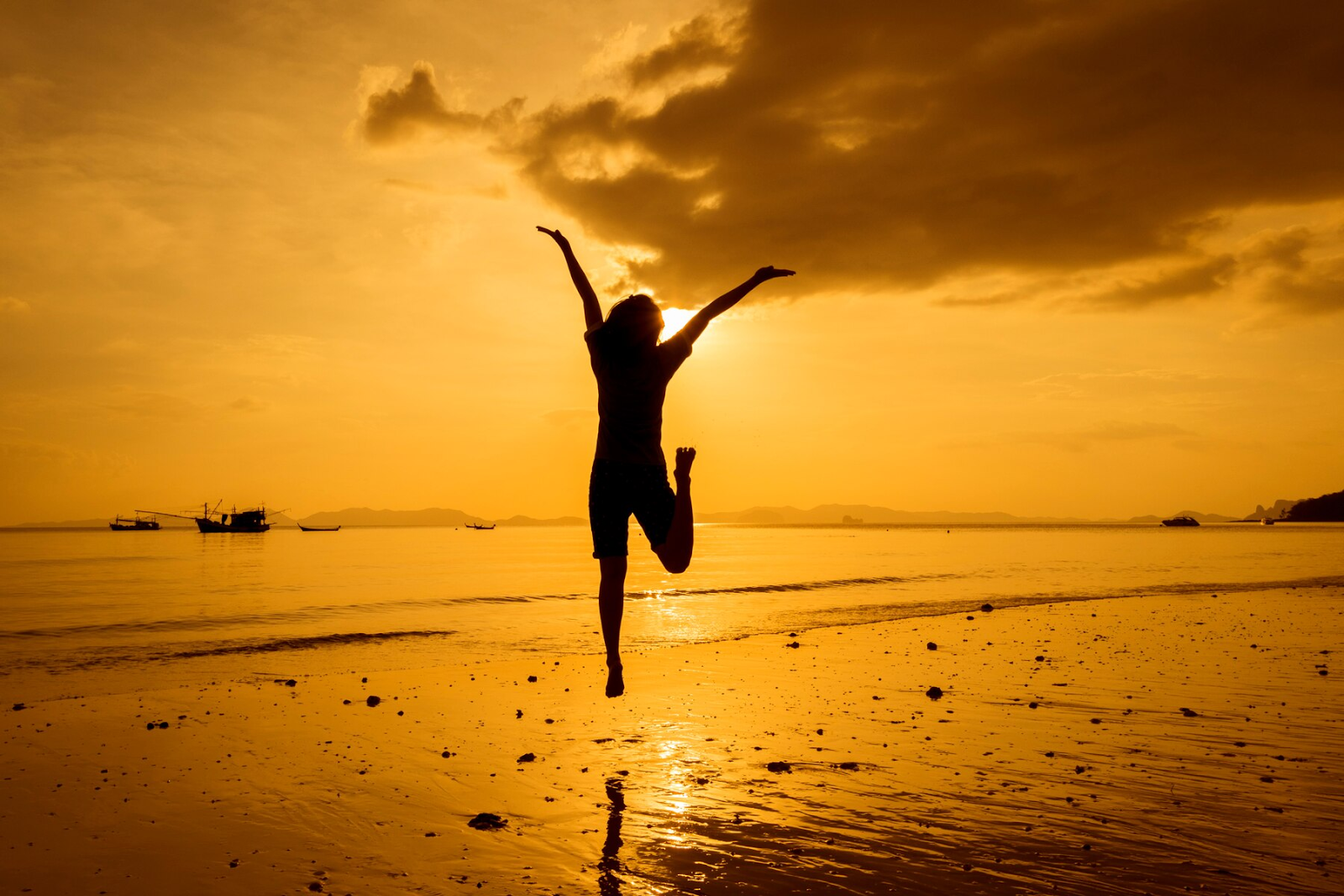 A woman jumping on the beach at sunset.