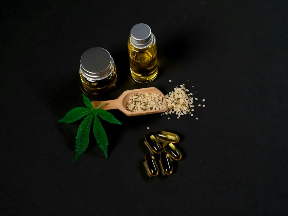 a cannabis leaf, two jars of CBD oil, CBD concentrate in a wooden spoon, and CBD capsules against a black background