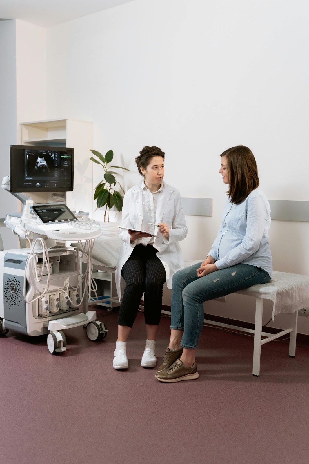 A doctor with a tablet consults a patient by an ultrasound machine in an exam room.