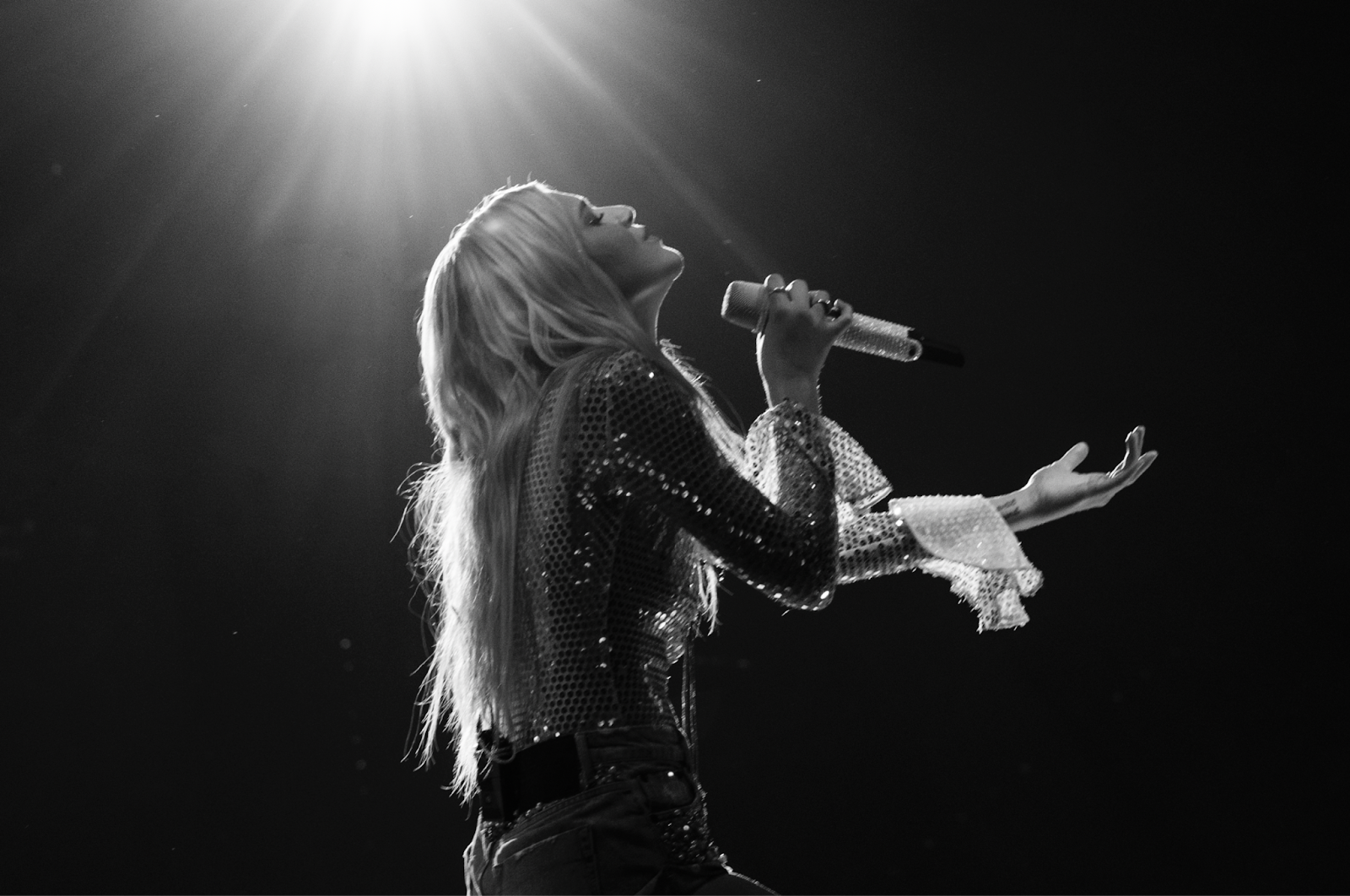 Black and white close up images of a blond, long-haired image looking upward towards a light, singing into a microphone. 
