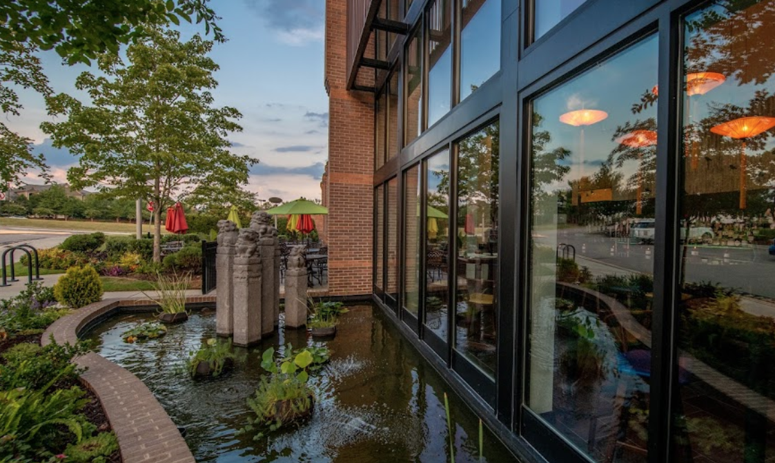 Exterior of G58 Cuisine, Chinese restaurant in Morrisville NC. Tall glass windows, koi pond and setting sun in the sky.