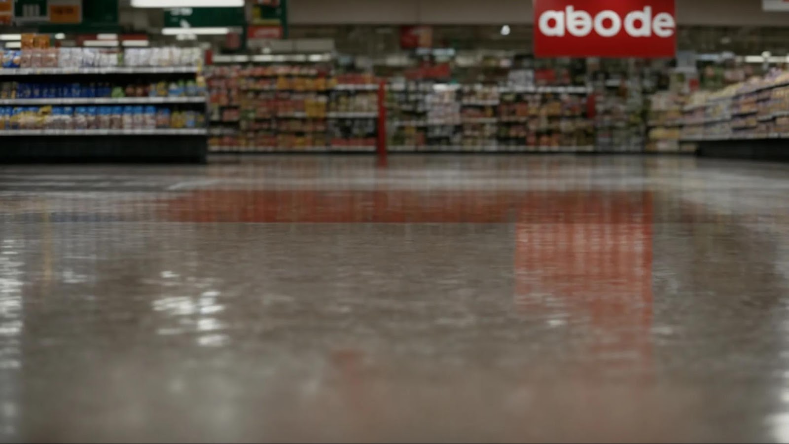a warning sign beside a wet floor inside a supermarket aisle.