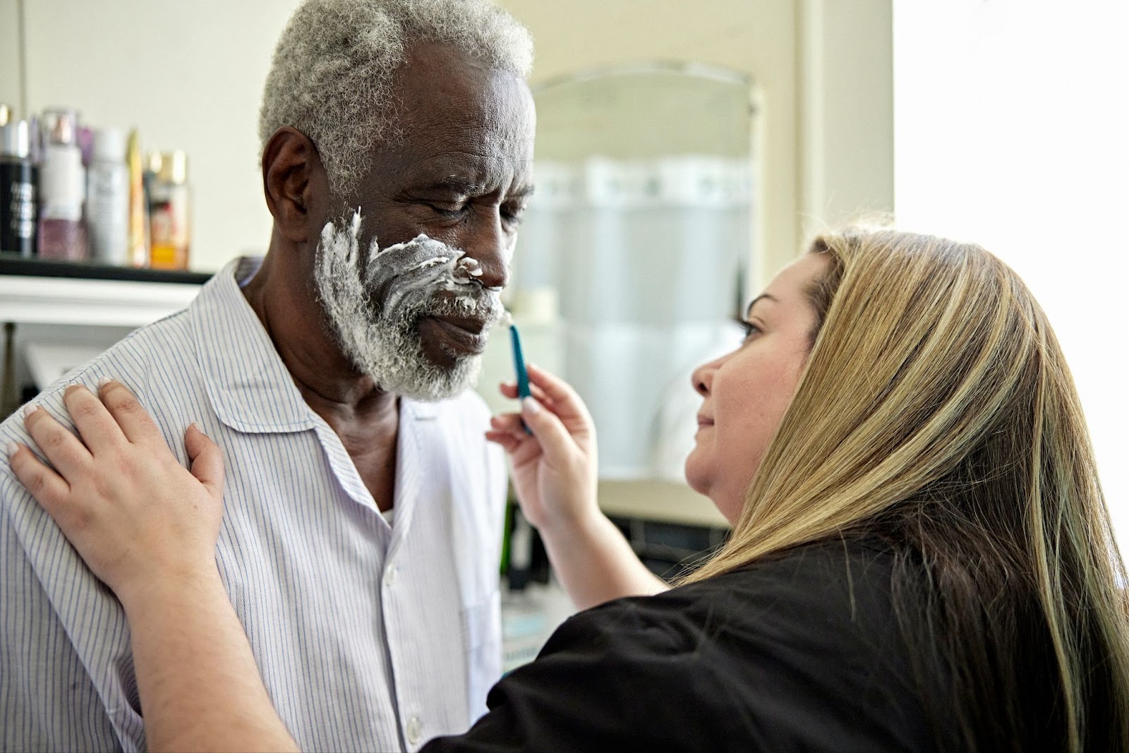 caregiver shaving senior man in beauty salon