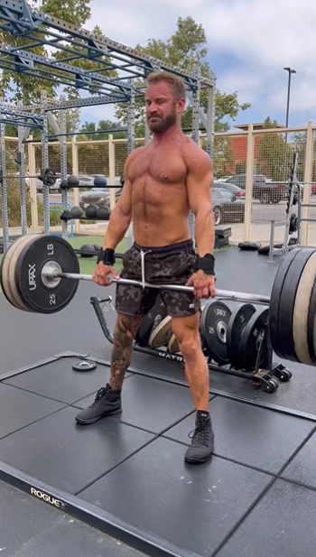 Bruce Jones dead lifting outside shirtless in an outdoor gym surrounded by plate weights