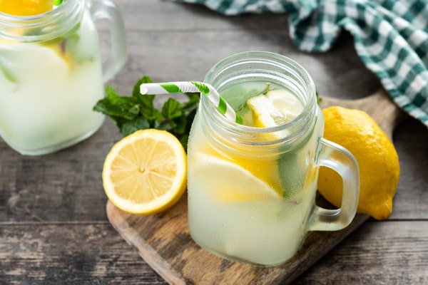 A jar of lemonade with straw and herbs, lemons on the side, and served on a wooden board