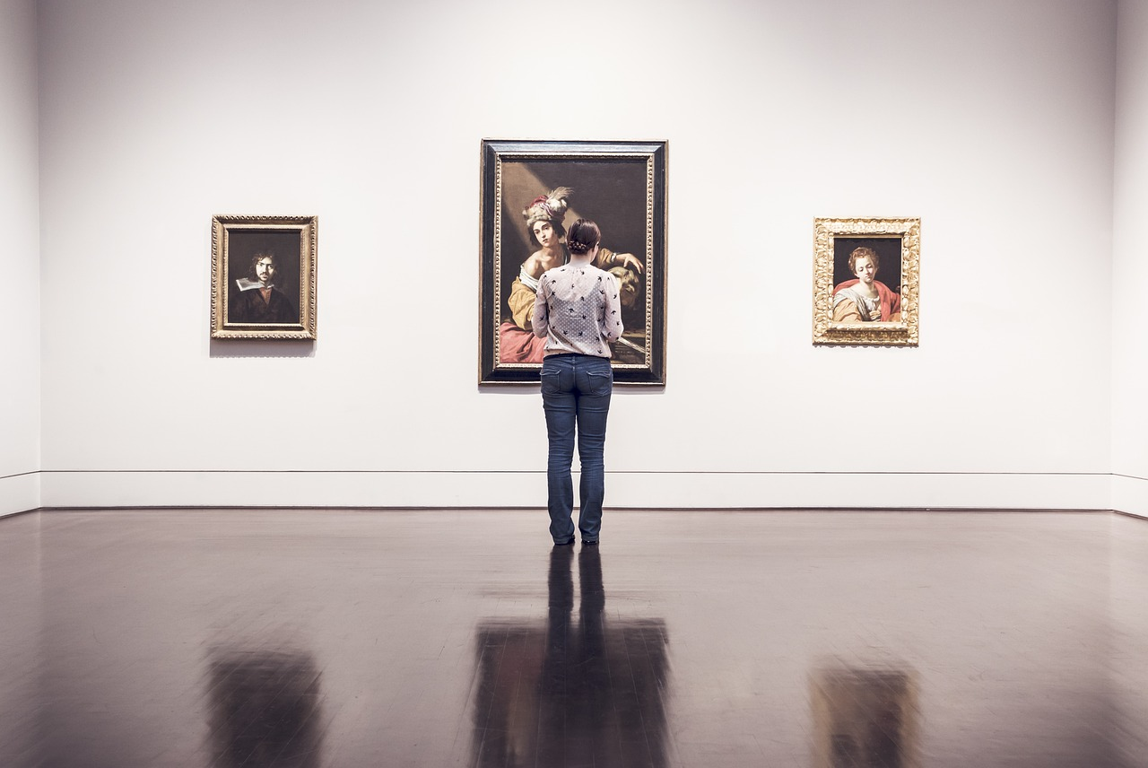 a gallery visitor standing in front of a row of three portrait paintings in a white gallery