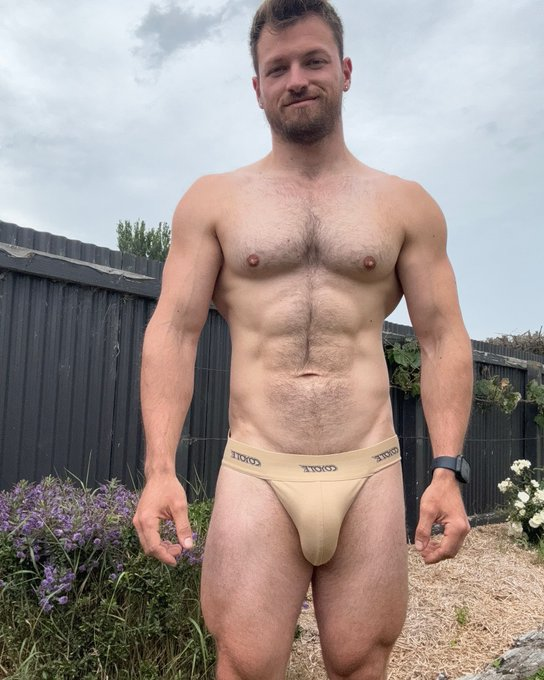 Max Small standing outside wearing nothing but his fleshtone jockstrap smiling for the camera