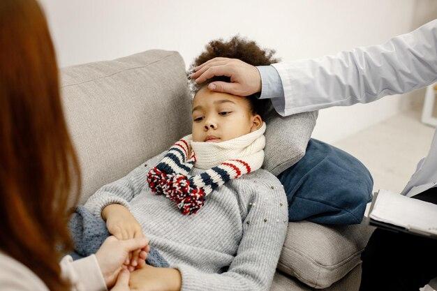 Free photo male pediatrician holding hand on a forehead of sick little black girl