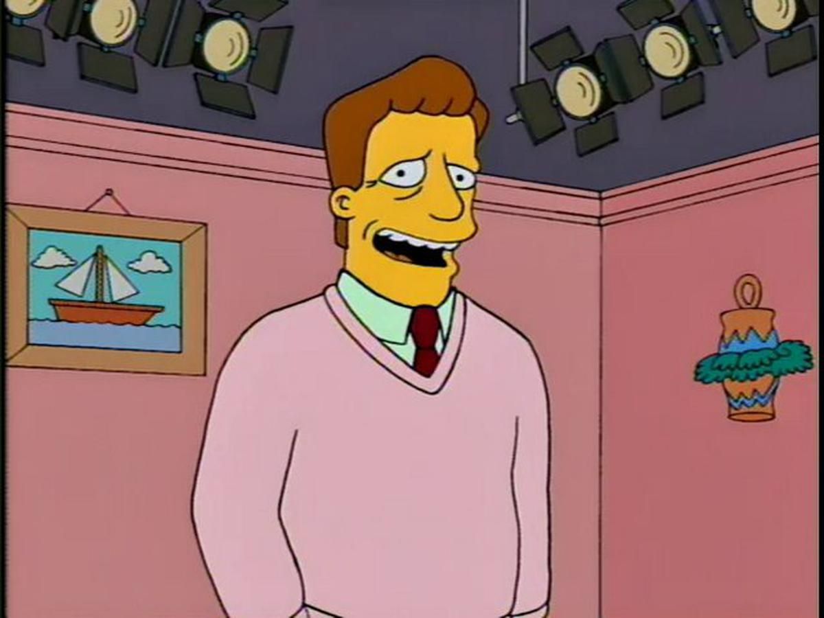 Troy McClure hablando ante la cámara en un set que asimila el living de la familia Simpson