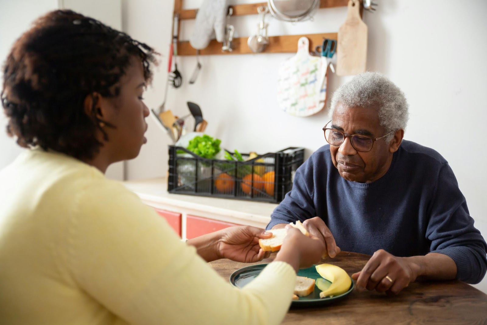A caregiver helping a senior citizen eat food from a plate in front of them