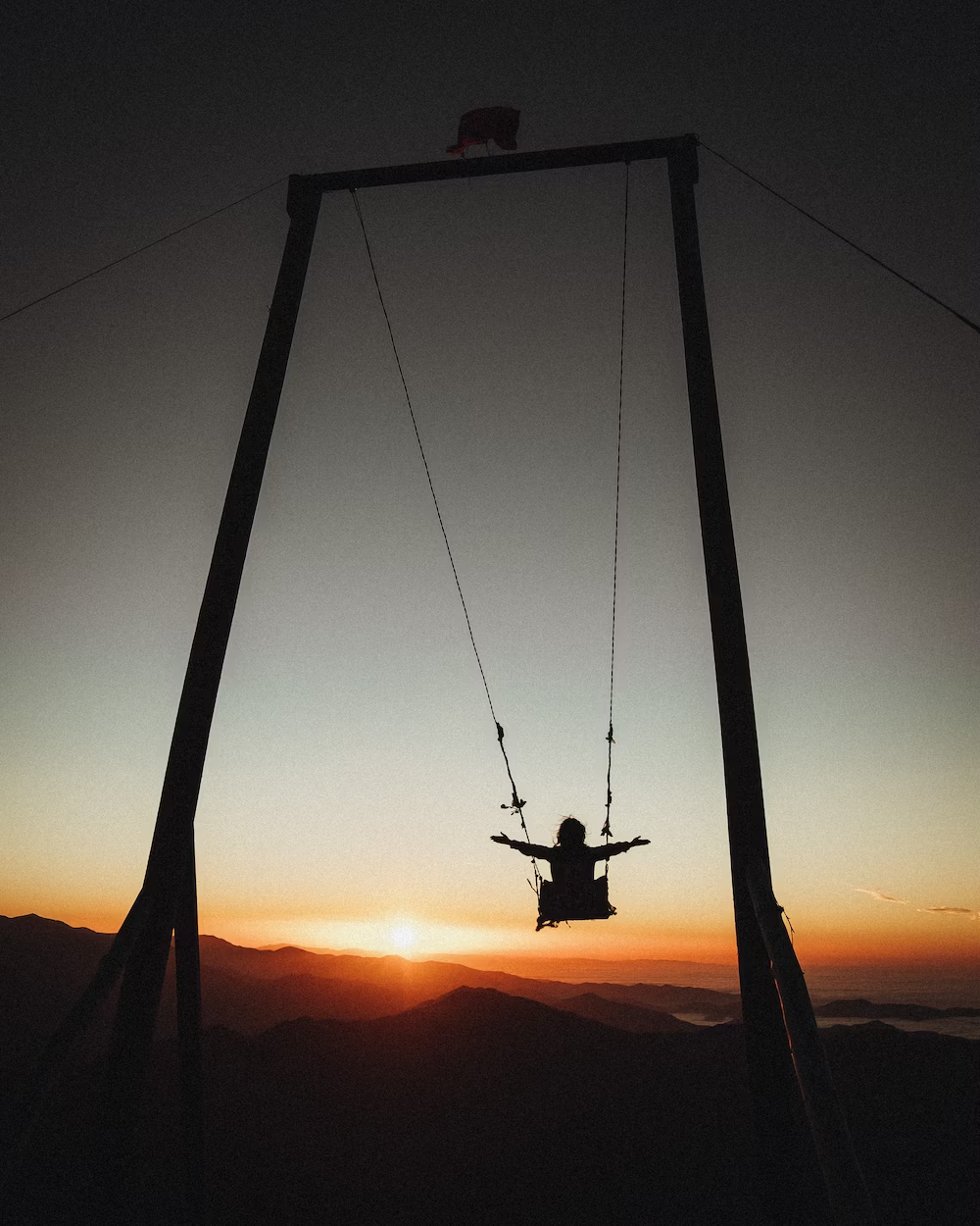 A Girl Enjoying a Swing With Hands in Air Against Sunset