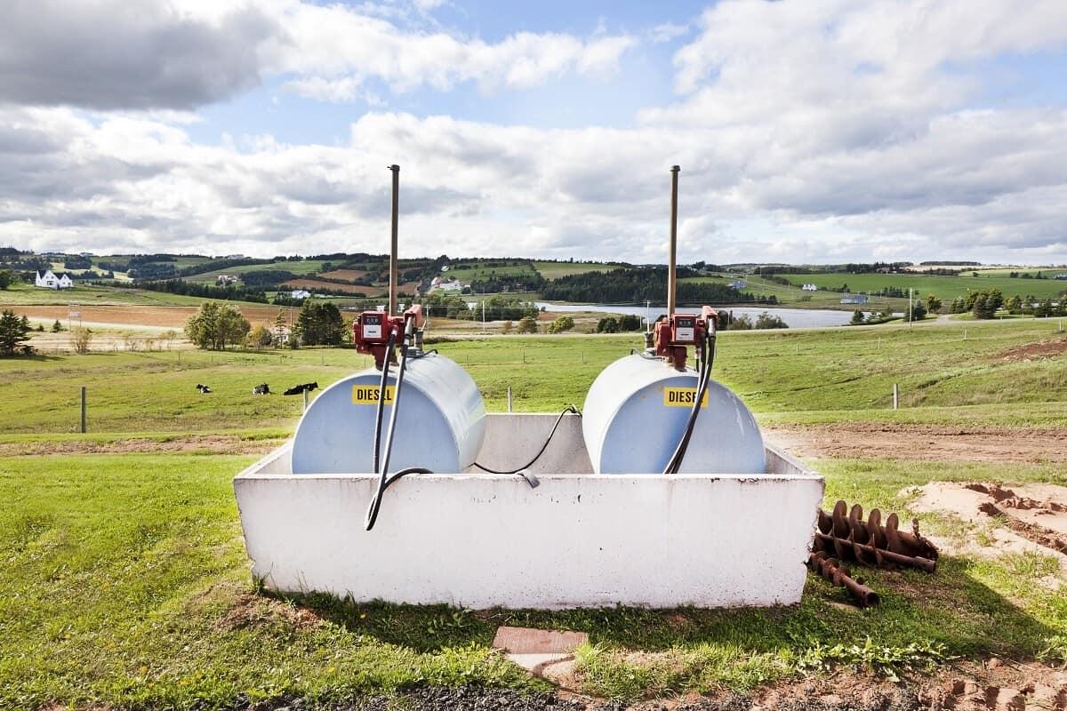 Tanque de armazenamento de combustível em uma fazenda. Há dois galões de diesel em um suporte de concreto, com um grande campo no fundo.