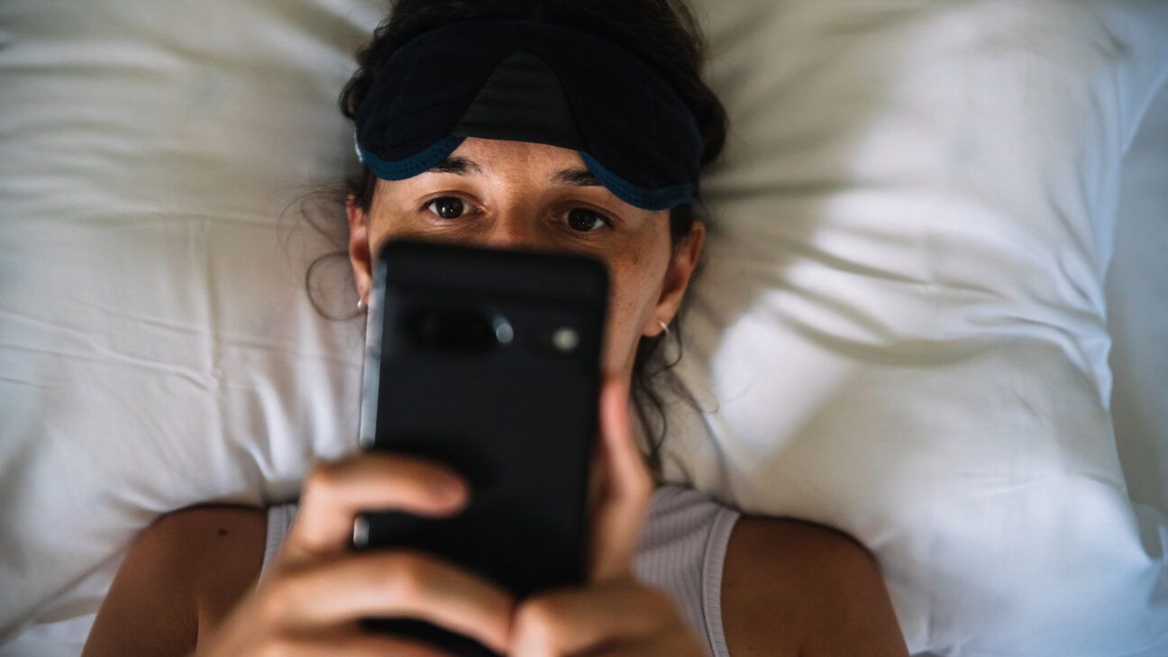 Woman looks at her phone in bed.