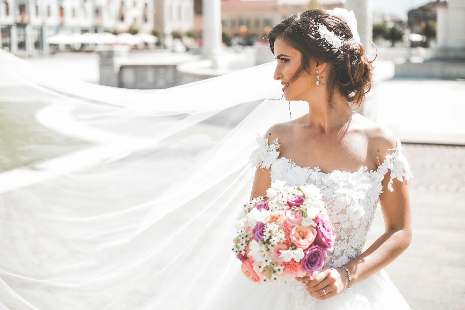 A bride walking along the shoreline, adorned in a lace wedding dress with off-the-shoulder straps, radiating classic elegance.