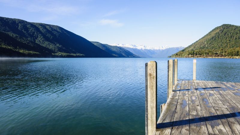 A wooden dock extends into a tranquil lake surrounded by steep mountains at Nelson Lakes National Park.