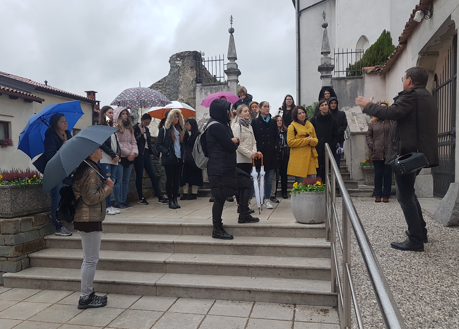 A group of people standing on stairs with umbrellas

Description automatically generated