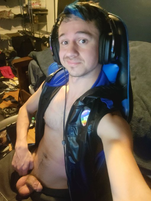 Dakota Wonders wearing a black and blue leather vest with his pants open jerking off in his gaming chair