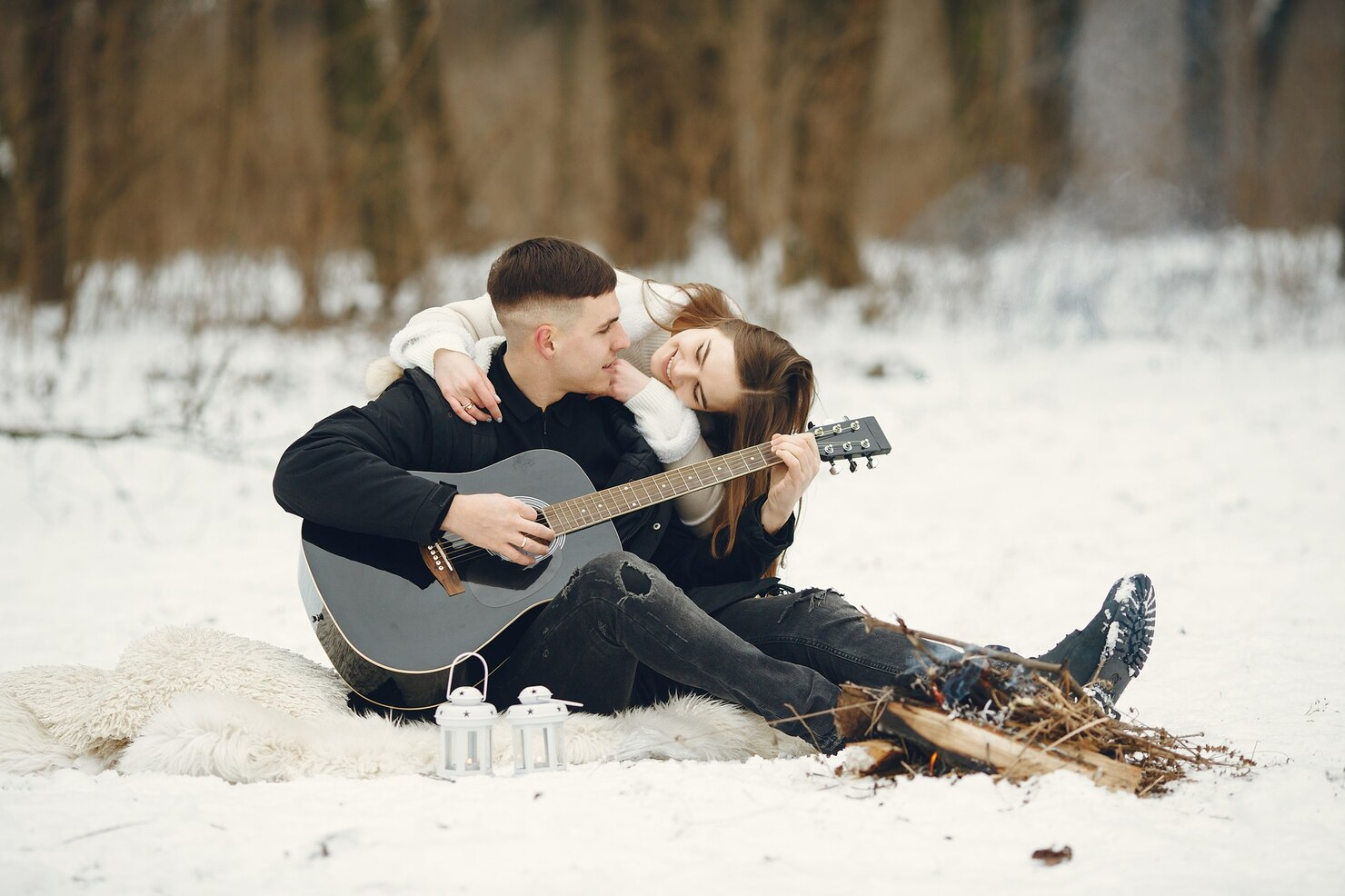A couple enjoying the winter while the man strums a guitar.
