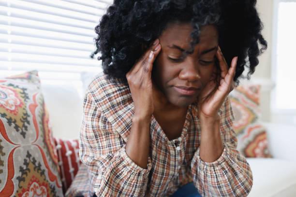 woman holds her head in pain - black woman stress stock pictures, royalty-free photos & images