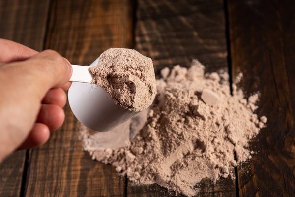 A person holding a teaspoon filled with protein powder
