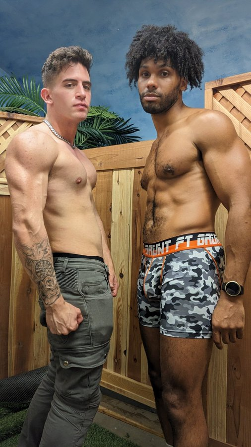 Tony Genius shirtless and wearing camo boxer briefs while posing with gay adult film content creator Trevor Brooks