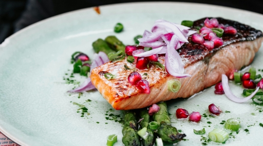 salmon decorated with onions and pomegranate seeds, served on a white plate