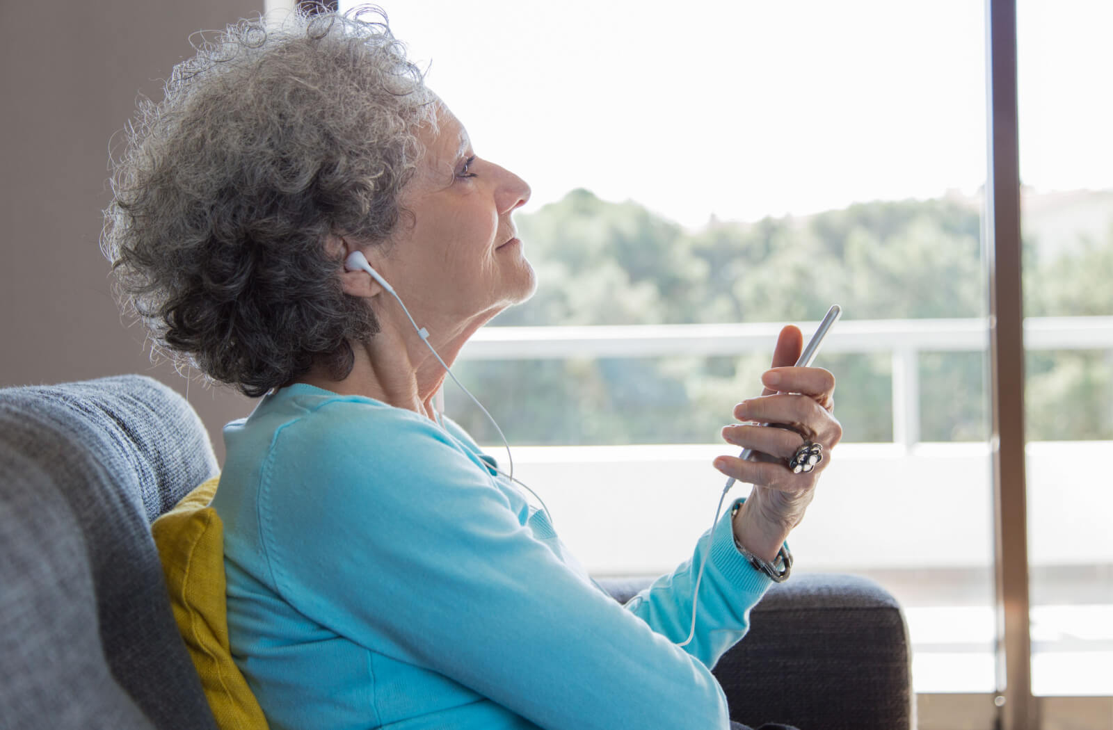A senior woman with curly hair happily listening to music.