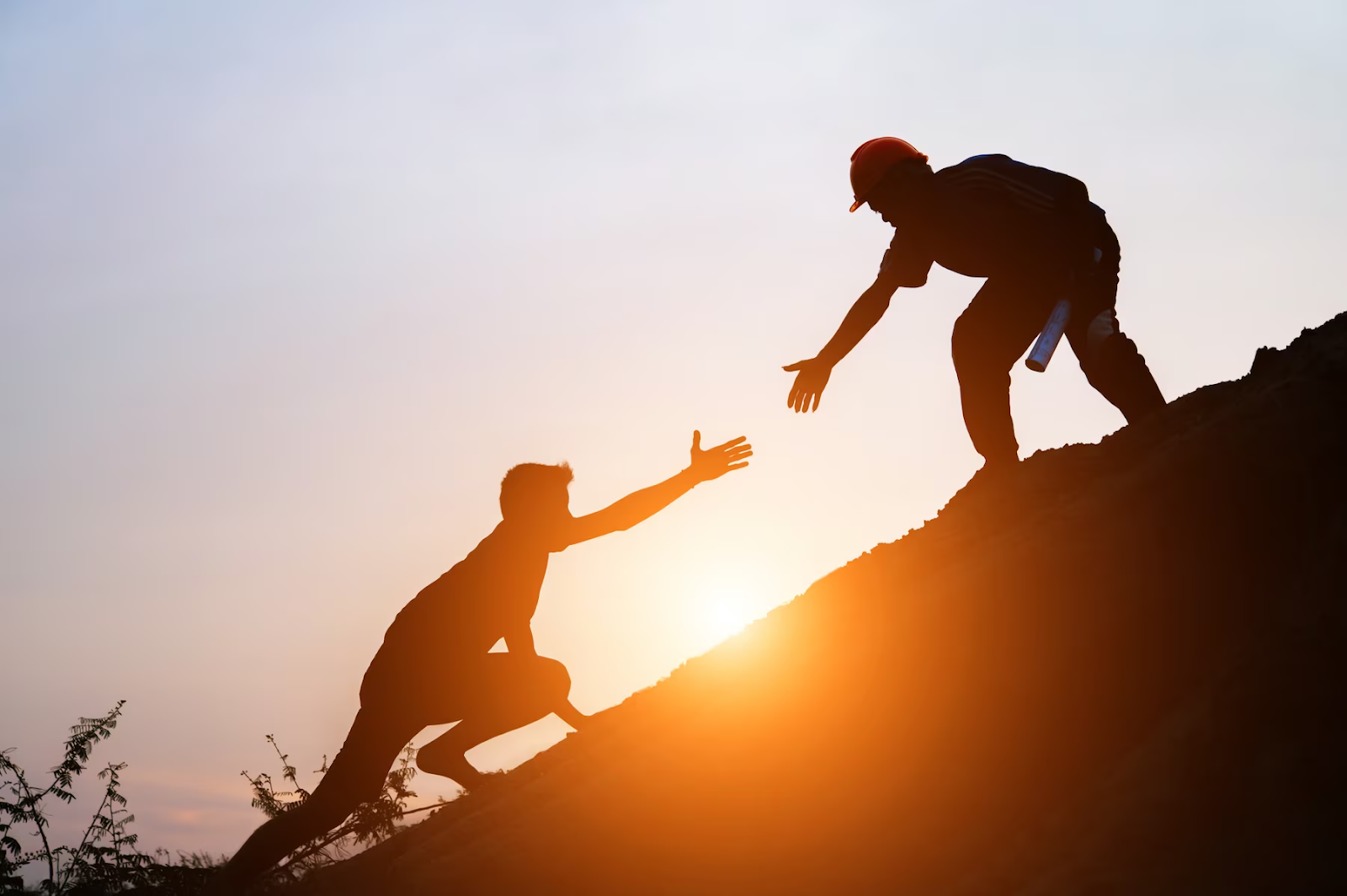 A man extending his hand to help a boy climb a hill. 
