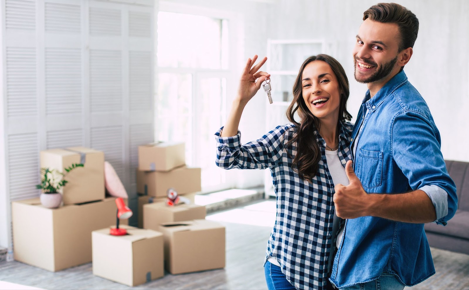 A couple smiling and holding up keys in front of their new home.