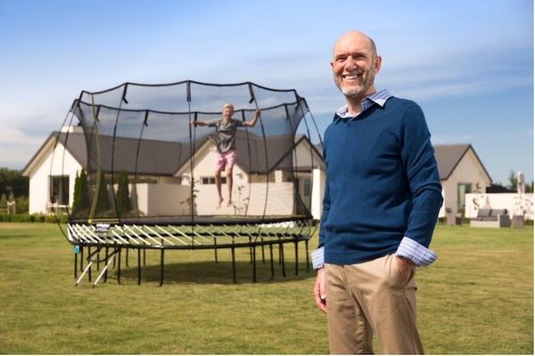 The inventor of Springfree Trampoline standing in front of a springless trampoline with a child jumping on it.