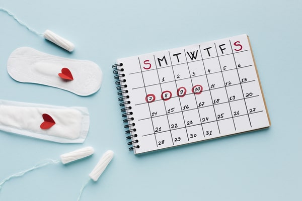 A calendar with red circles to resemble a menstrual cycle, with pads and tampons beside it