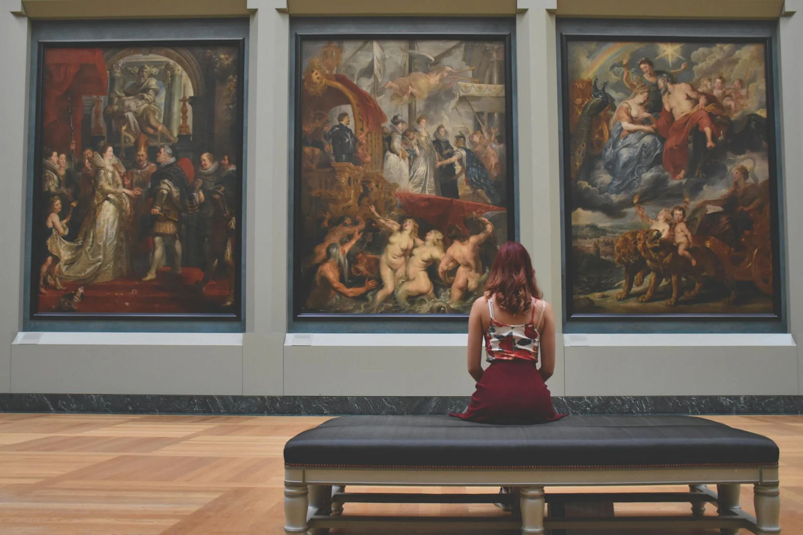 Women sitting on an ottoman in front of three paintings