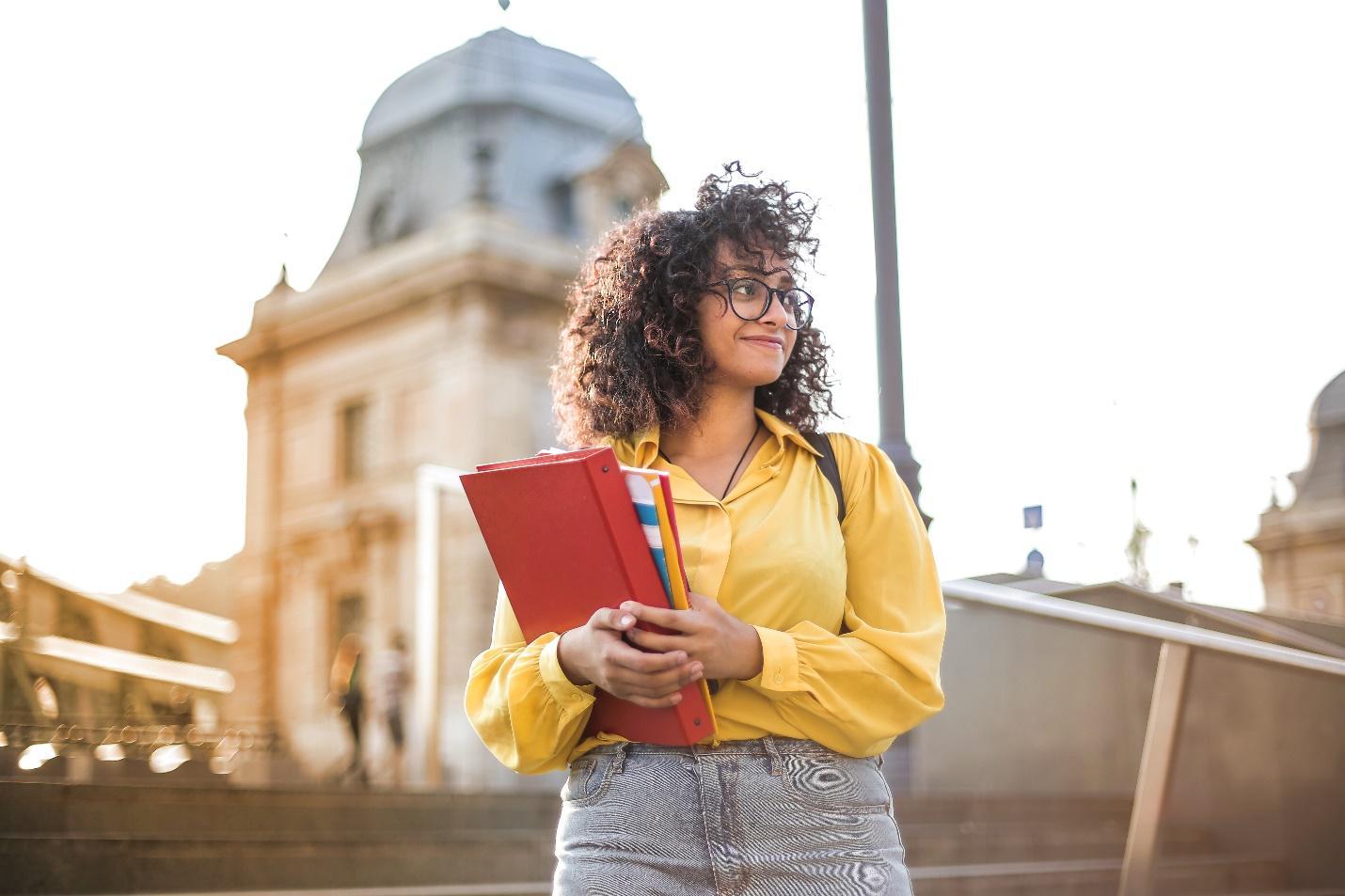 free woman in yellow jacket holding books stock photo