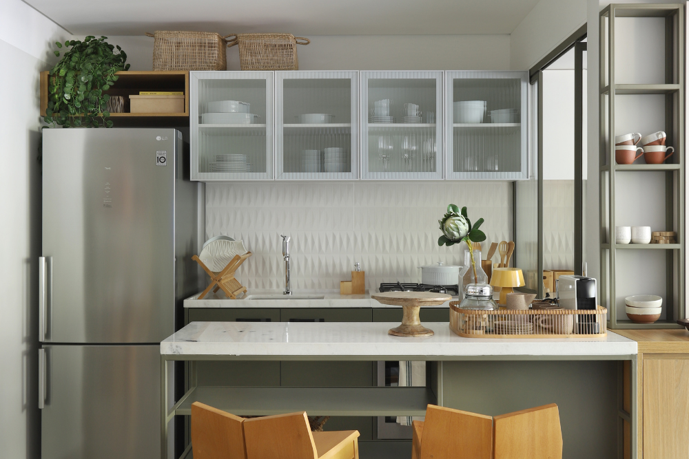 Cozinha pequena planejada com armários branco, móveis em inox, mesa branca com cadeira em madeira.
