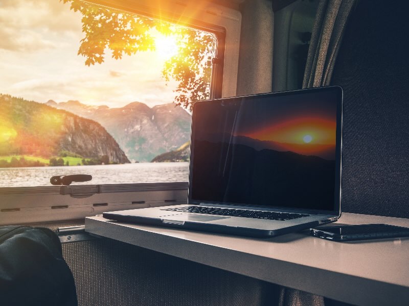 Laptop on a table in an RV with a lake and mountain outside the window - working from the road