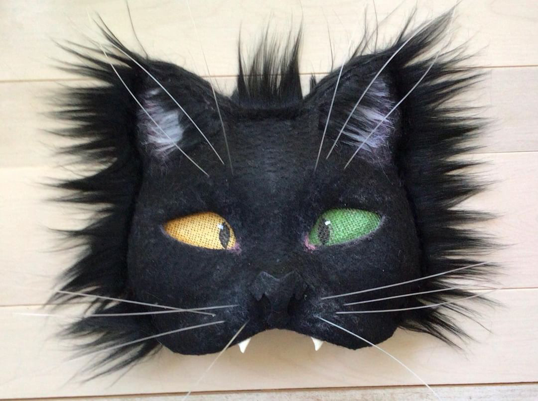 A black cat mask with one yellow eye and one green eye.