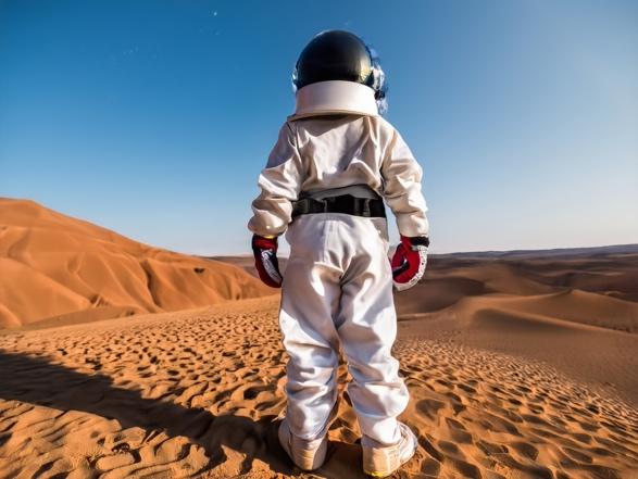 A person in a space suit standing in a desert

Description automatically generated