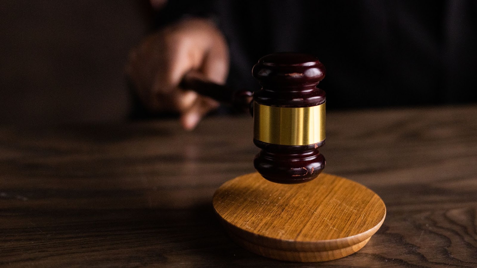 A judge's gavel in focus on a wooden block with the hand of a person in a dark suit blurred in the background, symbolizing a court's authority in legal matters.