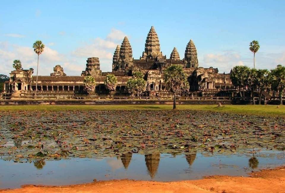 A large stone building with a pond in the background with Angkor Wat in the background

Description automatically generated