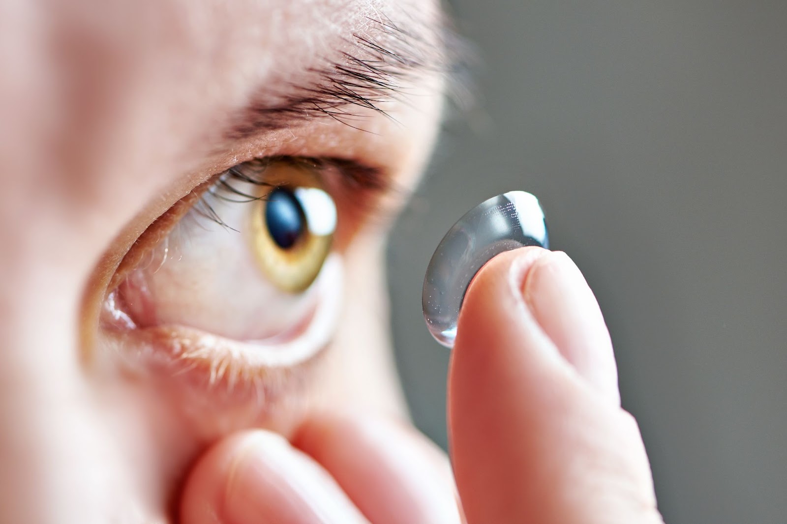 Close up picture of a person holding their eyelid down as they place a contact lens on their eye.
