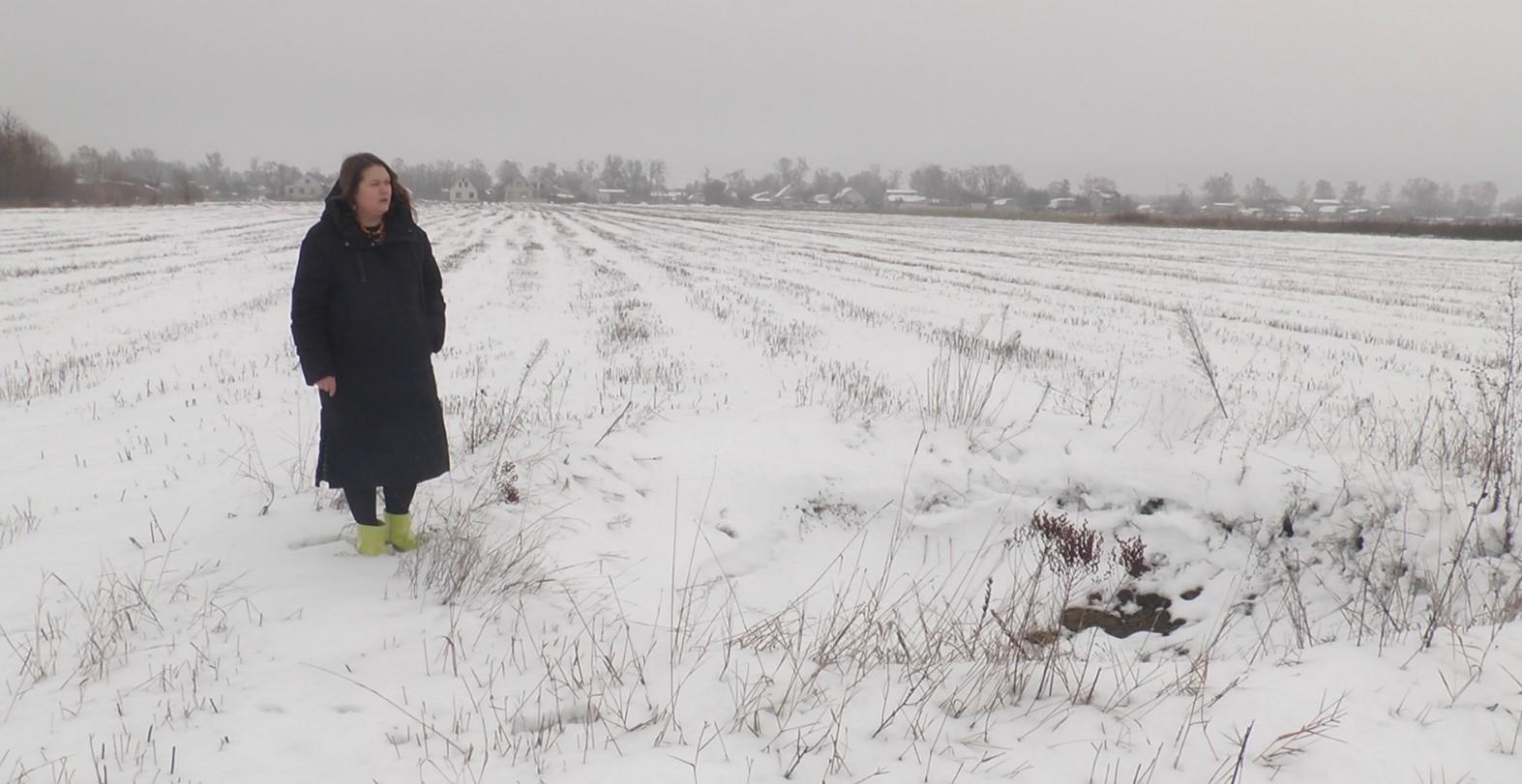 Тетяна Шанойло стоїть поруч з вирвою на полі, на якому її родина вже кілька років вирощує гречку та жито. Зараз її масштаби приховав сніг