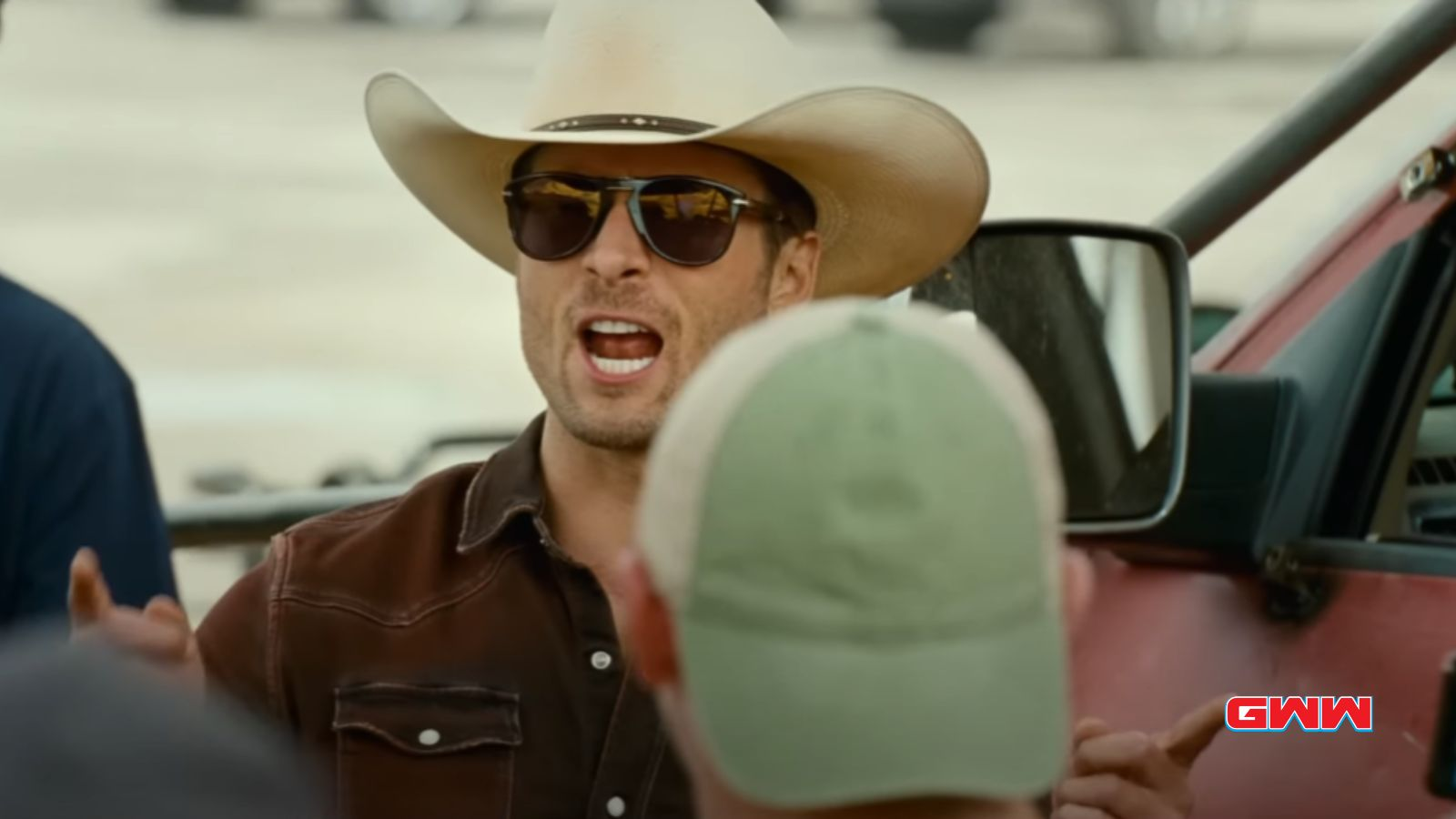 Tyler Owens wearing a cowboy hat and sunglasses, speaking passionately outdoors.
