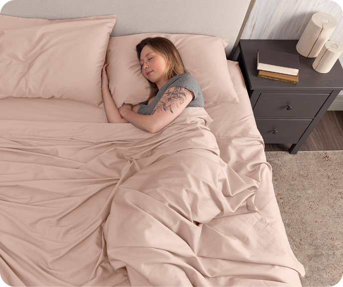 Our pink Organic Cotton Sheet Set in Rose Smoke shown on a bed with a female sleeping.