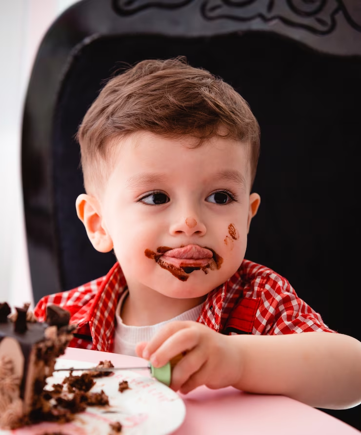 A little boy eats cake and gets chocolate on his face.
