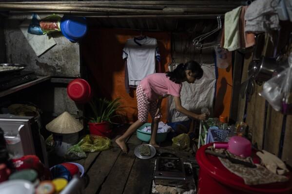 Do Bao Tran, who lives on a houseboat with her twin brother and their grandmother, grabs a cup in the kitchen in Can Tho, Vietnam, Wednesday, Jan. 17, 2024. After their mother left to pursue better financial opportunities in Ho Chi Minh City, the twins remained in the care of their grandmother, who supports the family by selling steamed buns at a floating market. (AP Photo/Jae C. Hong)