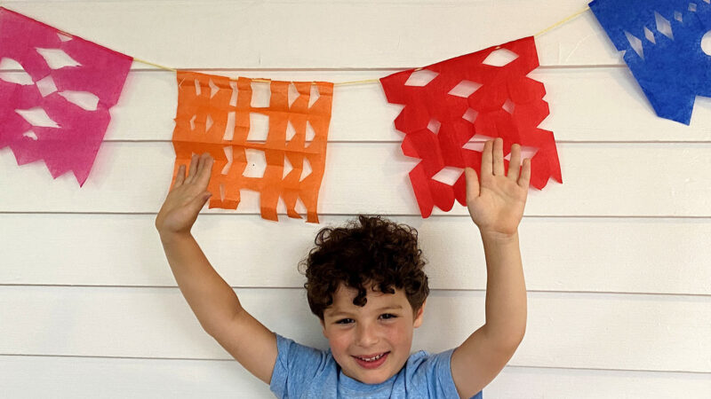 A child stands with his papel picado banner.