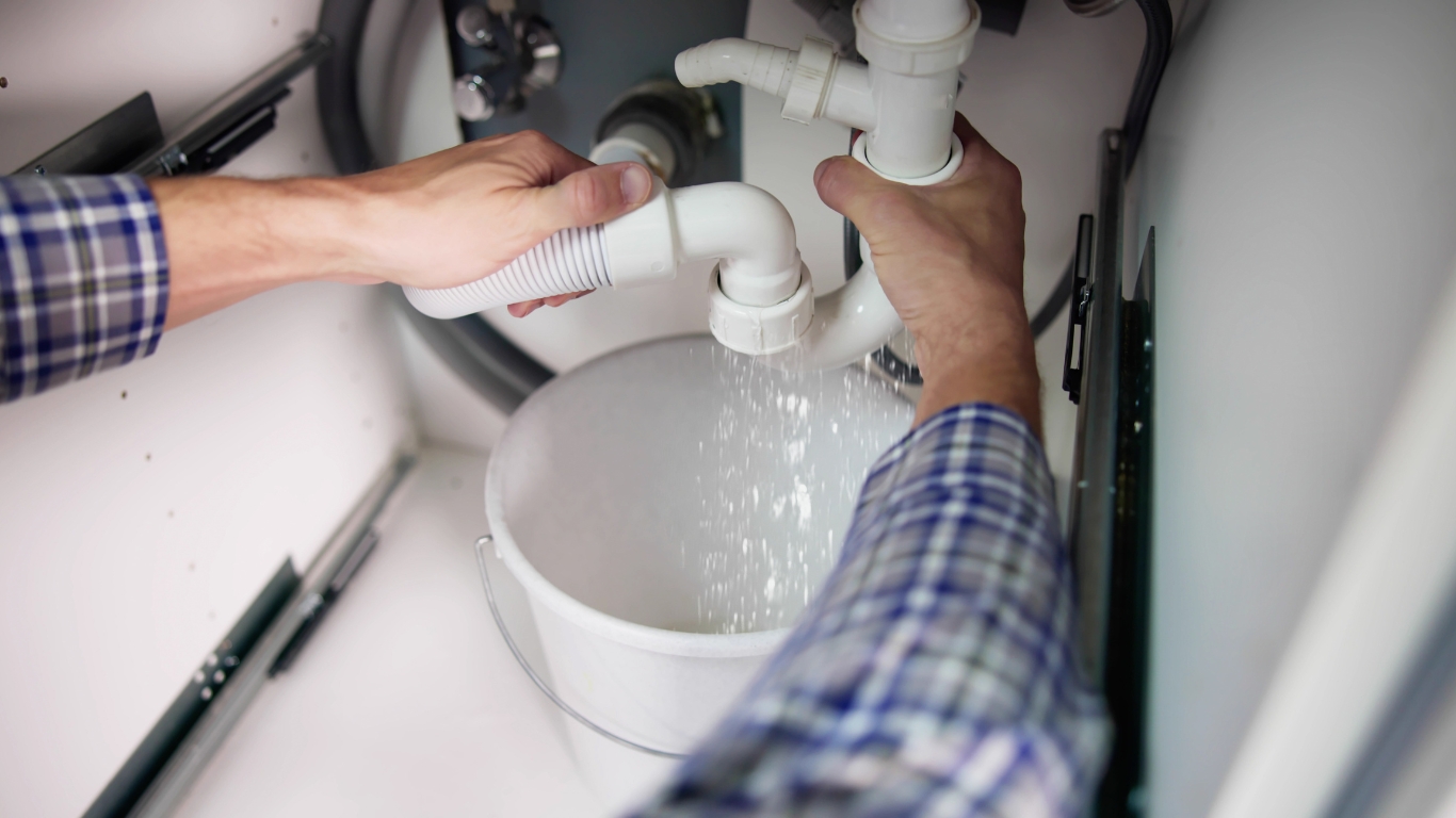 Plumber with fixing pipe while water dripping into bucket
