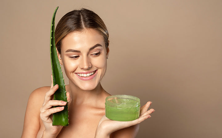 young female model holding aloe leaf and jar of aloe gel on beige