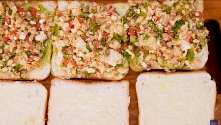 Buttered bread slices with chutney and vegetable-cheese mixture being layered for assembling the sandwich.